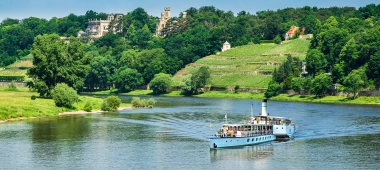 Ein Dampfschiff fährt auf der Elbe unter dem Blauen Wunder lang und ein Roter Doppeldecker überquert die Brücke.