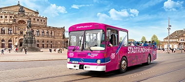 Gäste der Stadtrundfahrt fotografieren sich am Roten Doppeldecker vor der Semperoper Dresden.