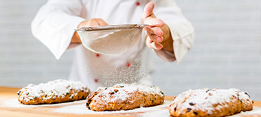 Zwei Bäcker vollenden einen original Dresdner Christstollen mit Puderzucker. Erleben Sie das Geheimnis des Dresdner Christstollen bei der Original Dresdner Stollentour